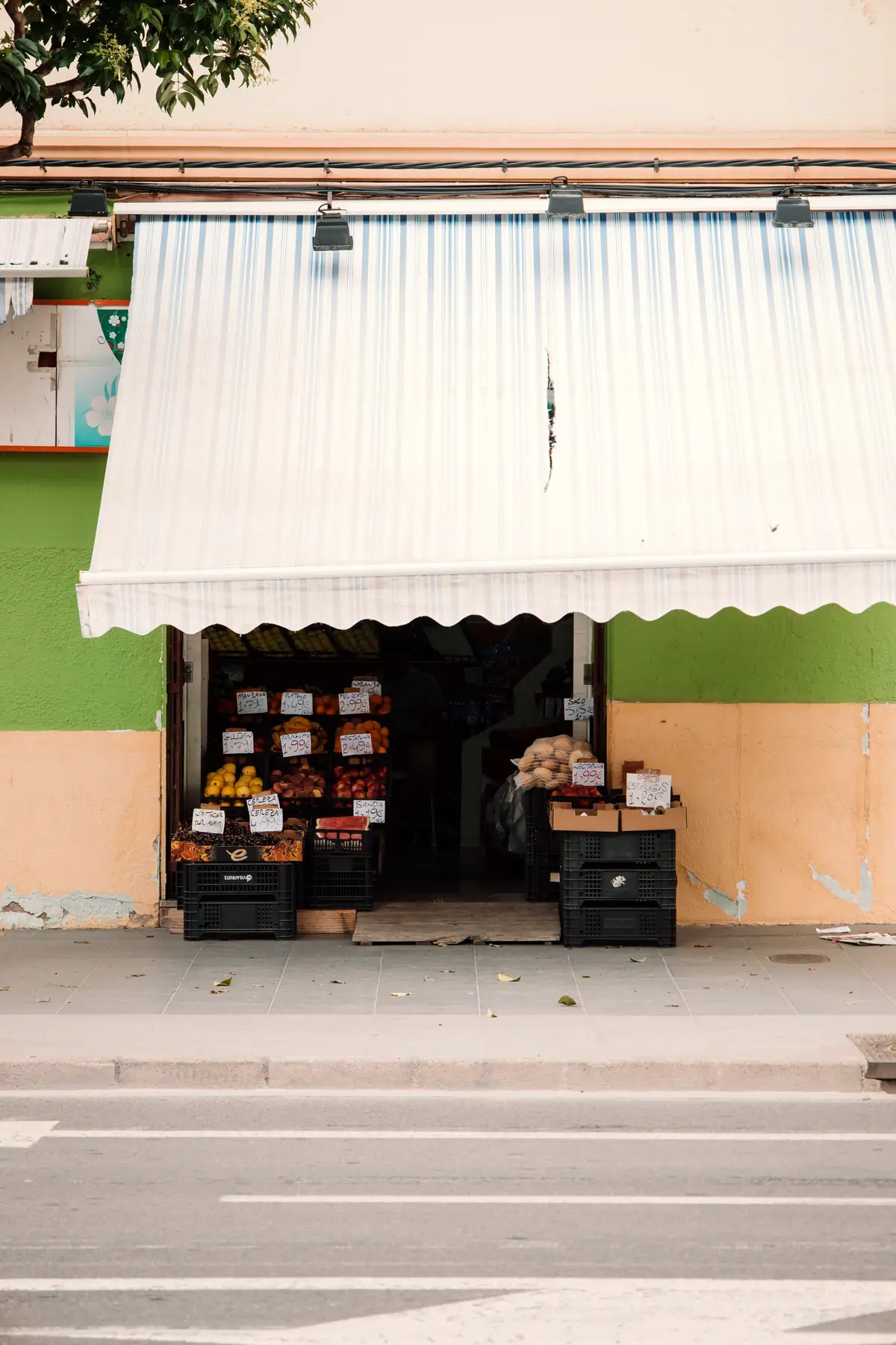 Fachada de una tienda de barrio con el toldo bajado y la mercancía en la puerta